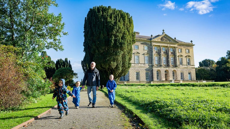 Three young children running to just beyond the front of the camera with an older gentleman running after them, at Castle Ward in autumn, County Down